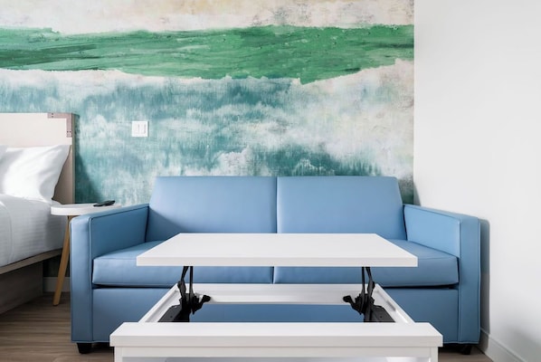 A room with a blue sofa, a white table, and a wall with a green abstract painting. - YourSpace Hotels Chesapeake (Chesapeake)