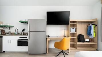 A compact hotel room with a kitchenette, a flat-screen TV, a desk, a chair, and a wardrobe.