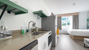 Una camera d'albergo moderna con angolo cottura, un letto, una finestra con tende e vista sull'esterno.