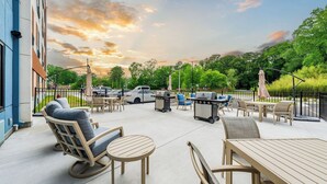 Una terrazza esterna con posti a sedere, un barbecue e vista su alberi e un edificio.