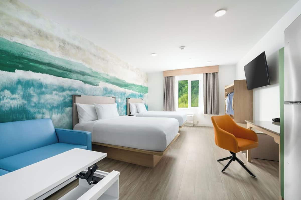 A hotel room with two beds, a blue sofa, an orange chair, a TV, and a window with curtains.