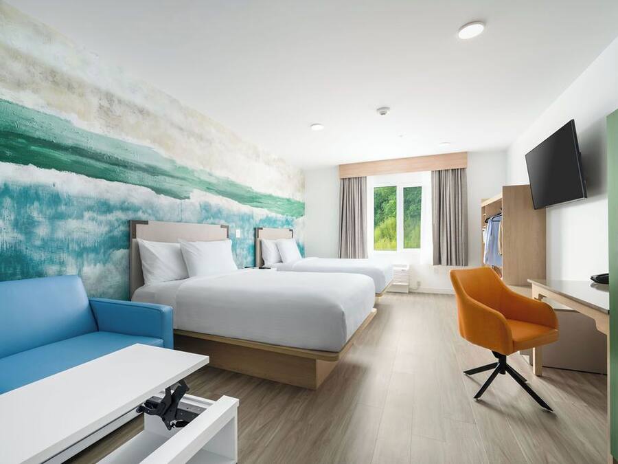 A hotel room with two beds, a blue sofa, an orange chair, a TV, and a window with curtains.