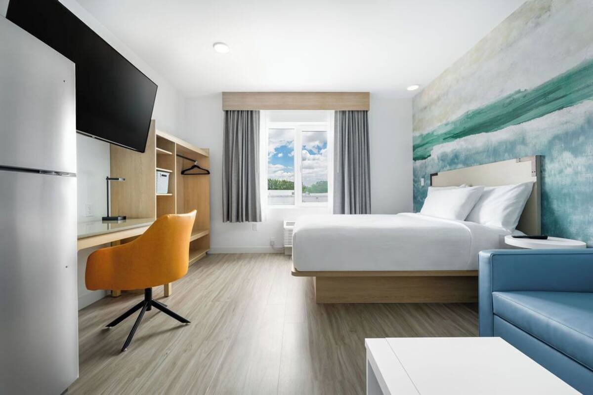 A hotel room with a bed, a desk, a chair, a TV, and a large window with curtains.