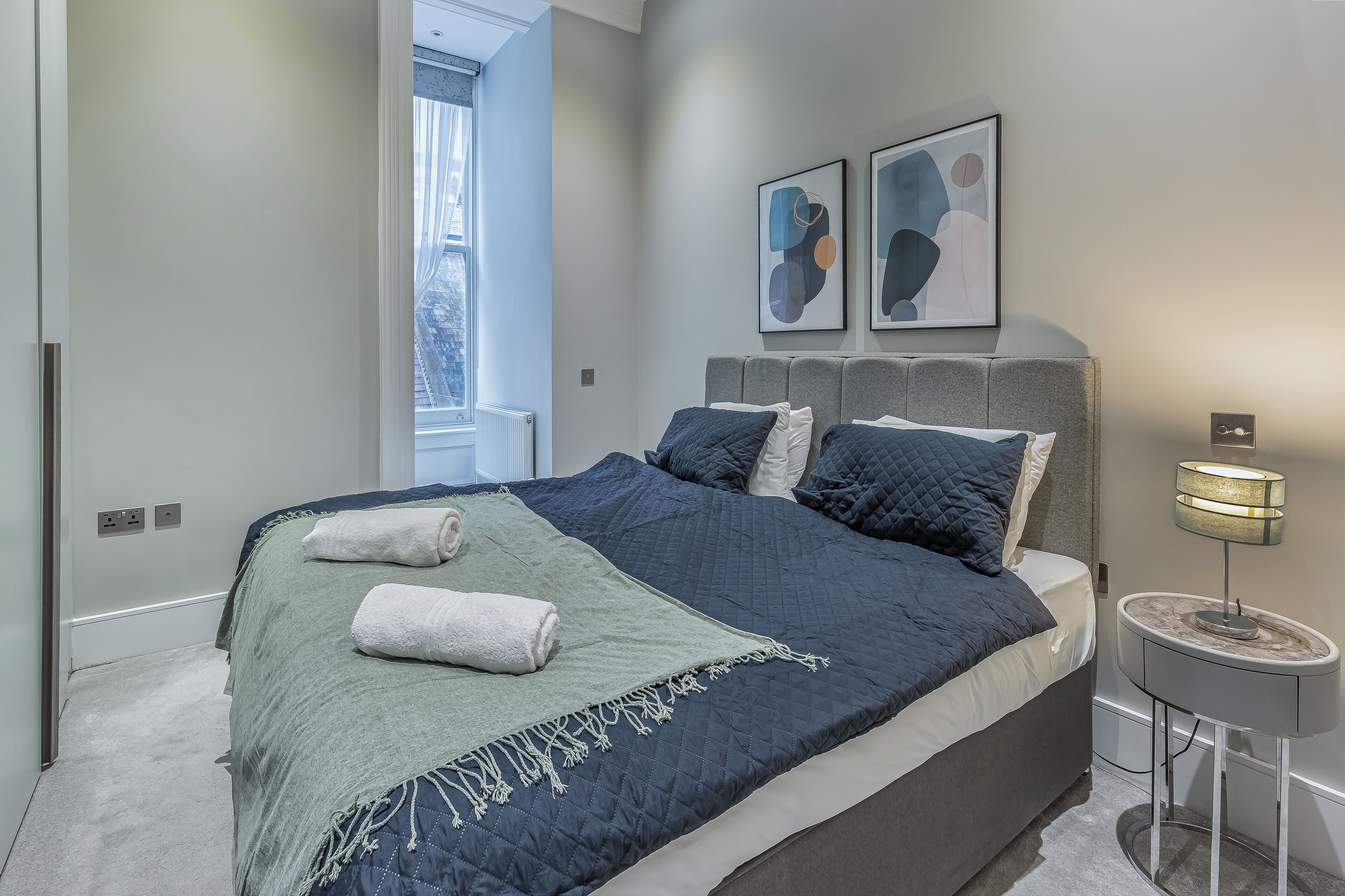 Ein Schlafzimmer mit einem großen Bett, einem Nachttisch mit Lampe und abstrakter Wandgestaltung.