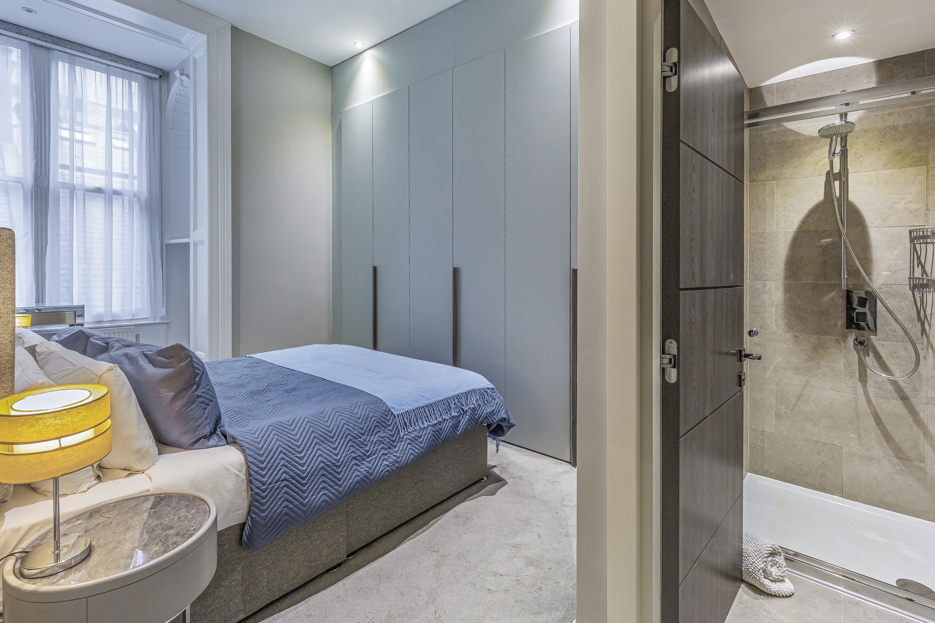A modern bedroom with a bed, bedside table, and a shower area.