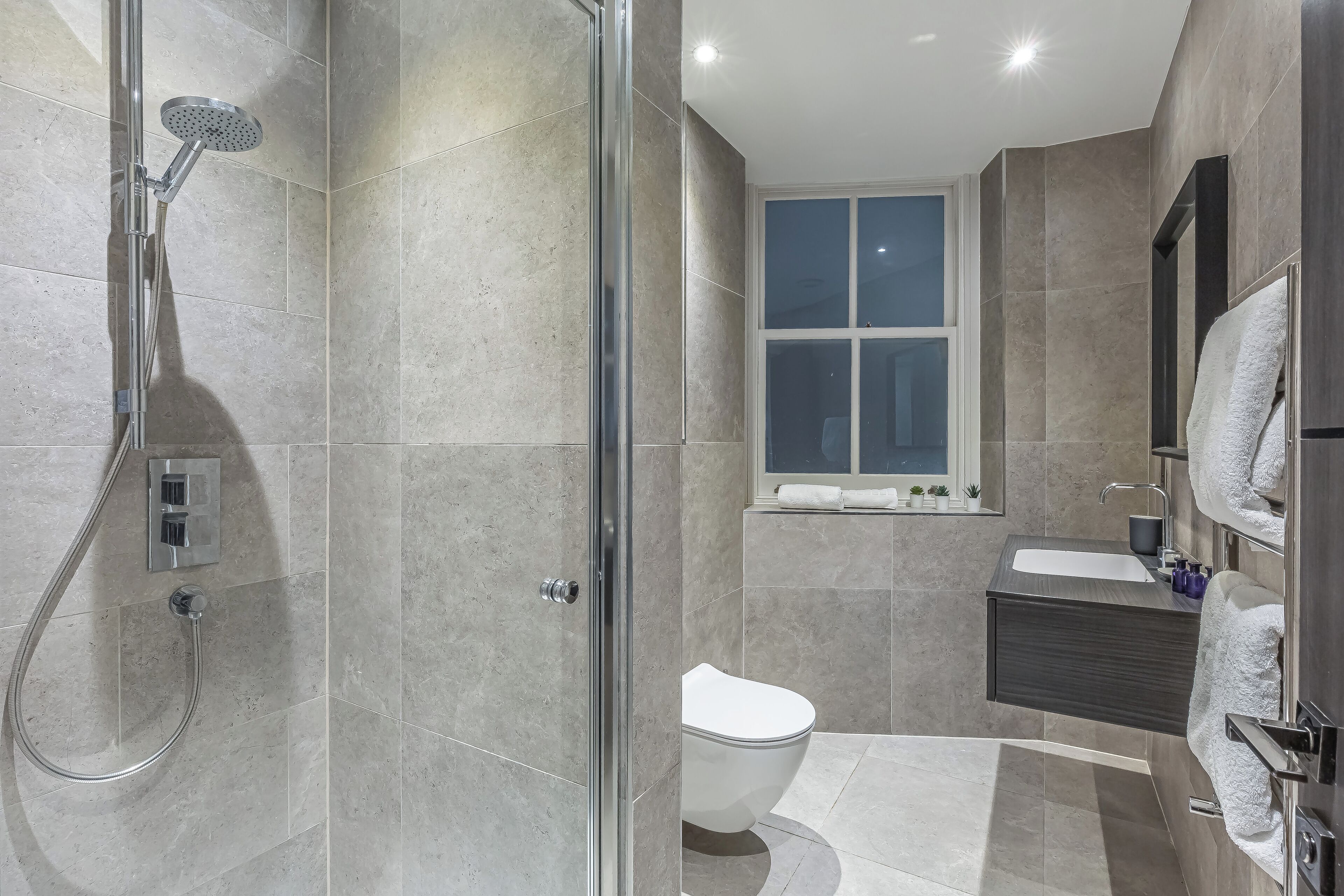 Un baño moderno con ducha de vidrio, inodoro blanco y tocador con espejo y lavabo.