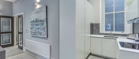 A modern kitchen with white cabinets, a large window, and a contemporary art piece on the wall.