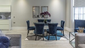 Un espace repas moderne avec une table en verre, des chaises à revêtement bleu foncé et un vase rempli de fleurs violettes.