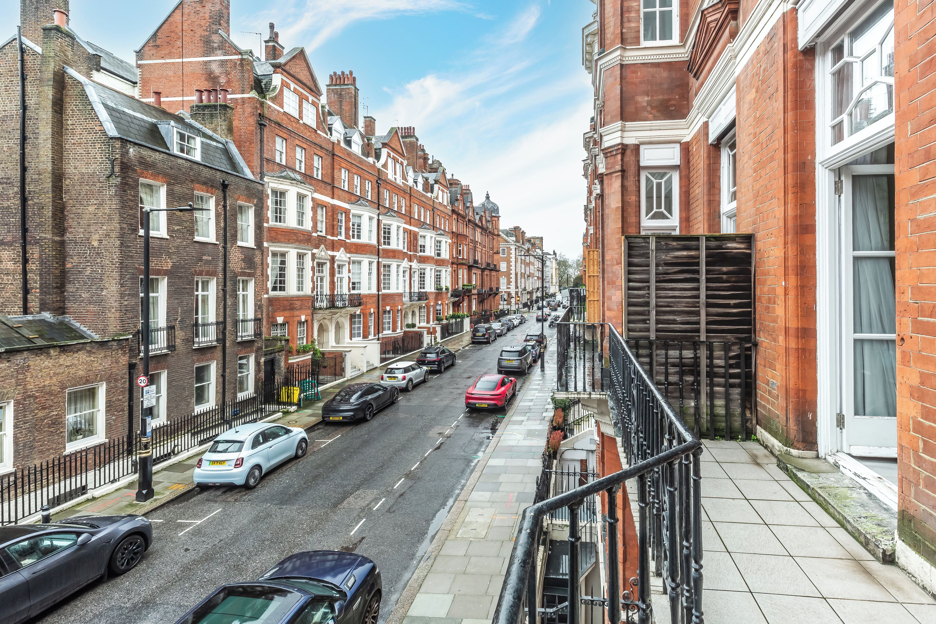 A street view of terraced houses with cars parked along the side.