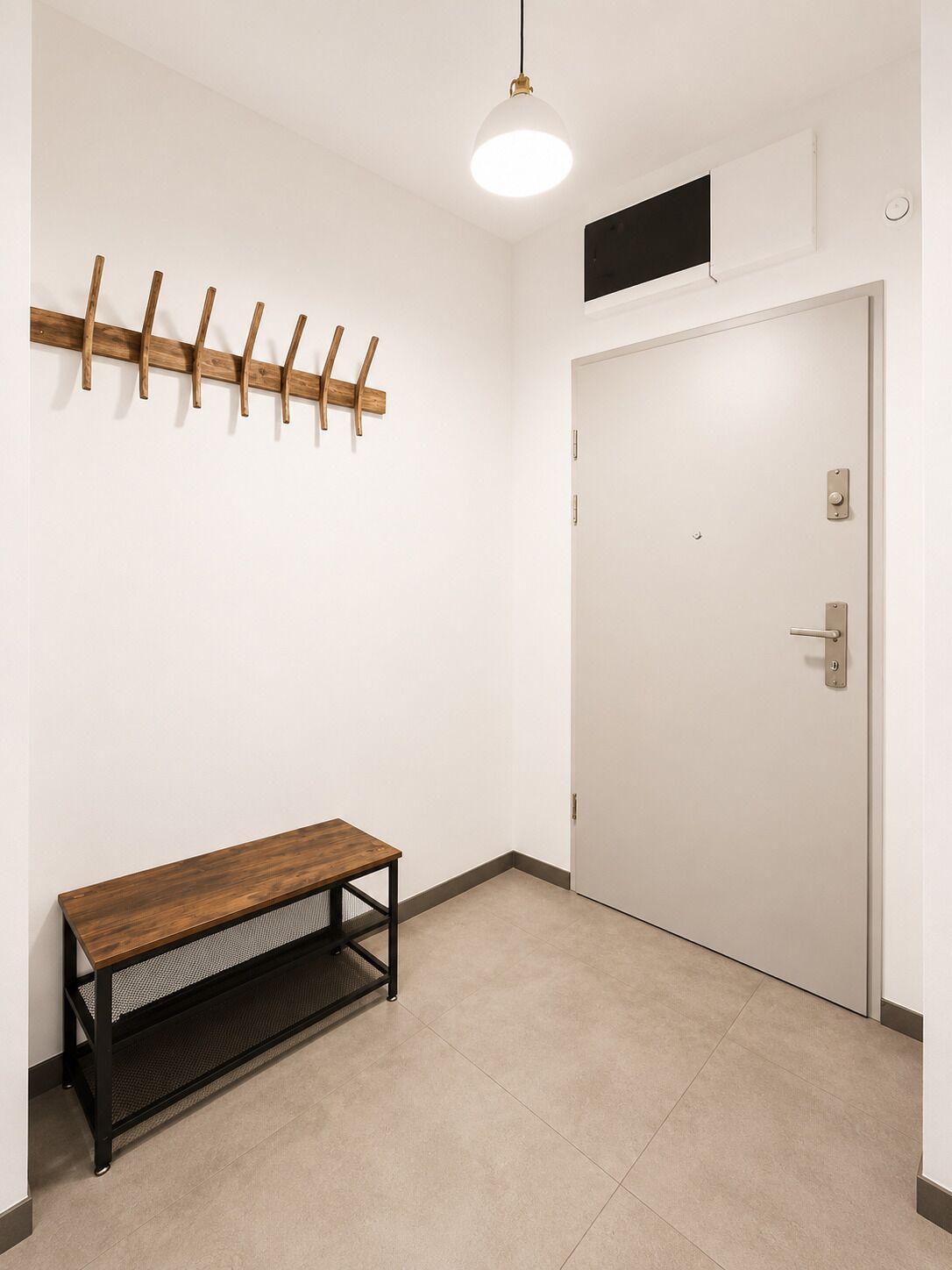 A room with a wooden bench, a coat rack, a white door, and a ceiling light fixture.