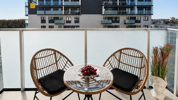 A balcony with two wicker chairs and a glass table, overlooking a modern building with balconies. - Lumina stylish apart near Pasaż Łódzki (Lódz)