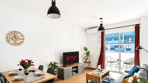 A modern living room with a dining area, a TV displaying 'NETFLIX,' and a view of a building through large windows. - Lumina stylish apart near Pasaż Łódzki (Lódz)