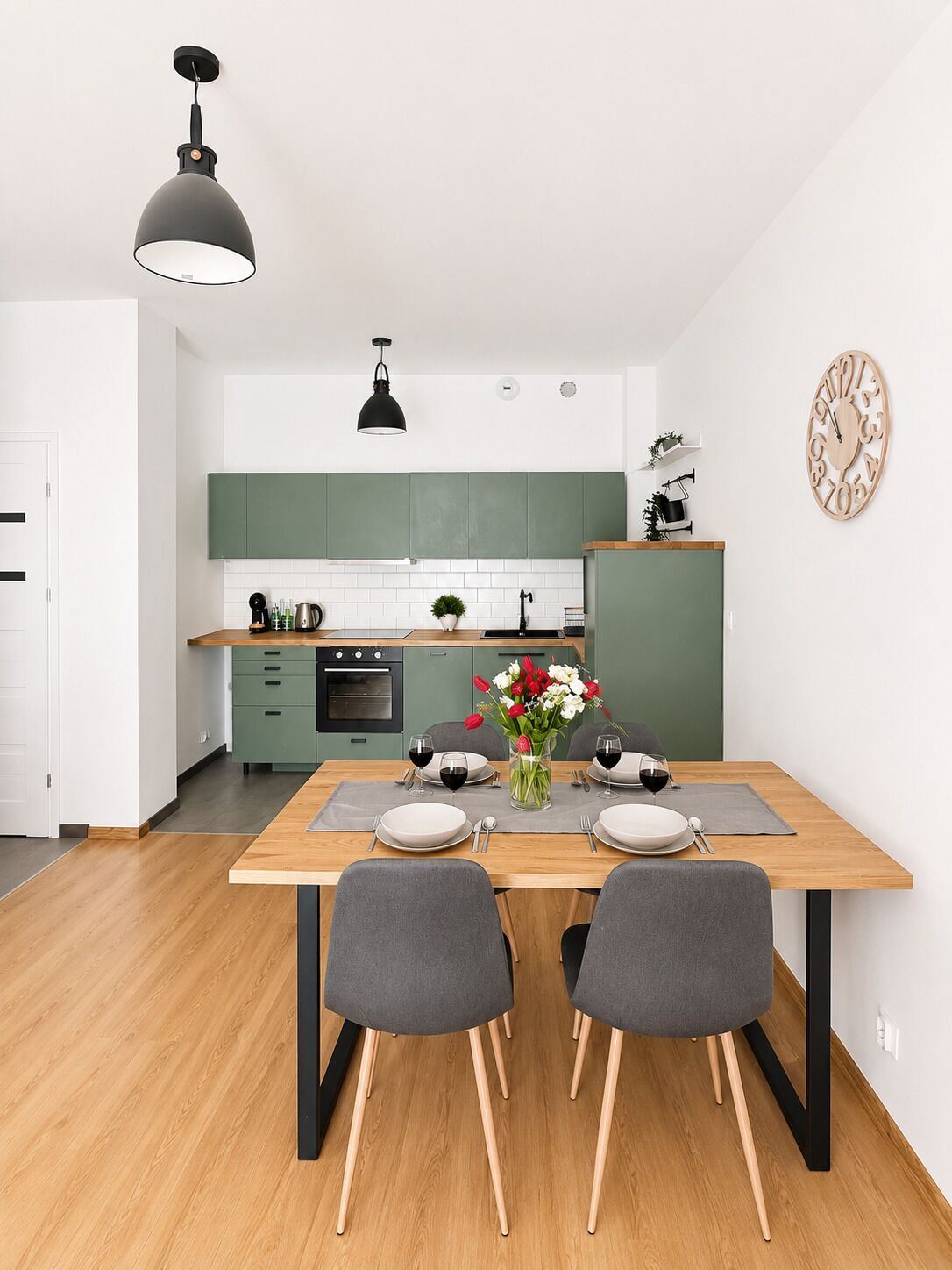 Una cocina moderna con armarios verdes, una mesa de comedor de madera con sillas e iluminación colgante.