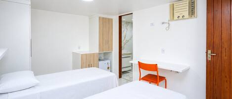 Une chambre d’hôtel avec deux lits simples, une armoire en bois, une petite table avec une chaise et un radiateur encastré.