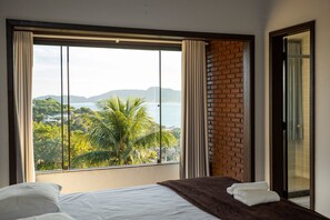A bedroom with a large window offering a view of a lush landscape and the sea.