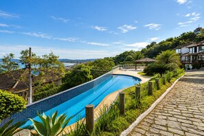 A swimming pool with a curved design, surrounded by lush greenery and a cobblestone path.