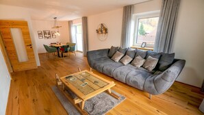 A modern living room with a grey sofa, wooden flooring, and a dining area with a table and chairs.