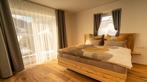 A bedroom with a wooden bed, a large window with sheer curtains, and a view of a snowy landscape.