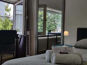 A hotel room with a bed, a chair, a radiator, a window with a view of trees, and a box labeled 'Caluxio Snickers'. - Charming Maya Room Close to City Center & UMCG (Groningen)
