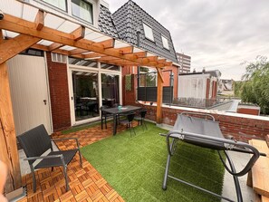 Een terras met een tafel, stoelen, een barbecue en een pergola.