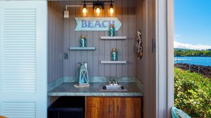 Cocina compacta con un lavamanos, un cartel que dice 'BEACH' y frascos decorativos en estantes.
