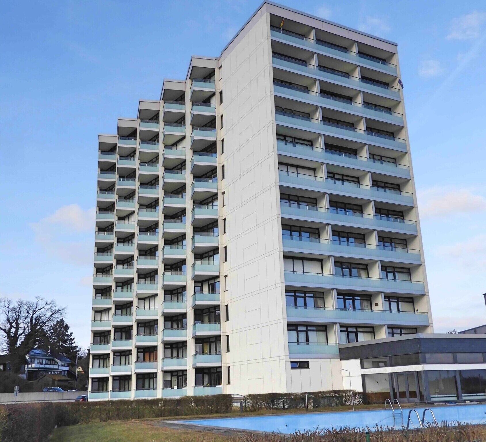 Ein Hochhaus mit mehreren Balkonen, einem Swimmingpool und blauem Himmel.