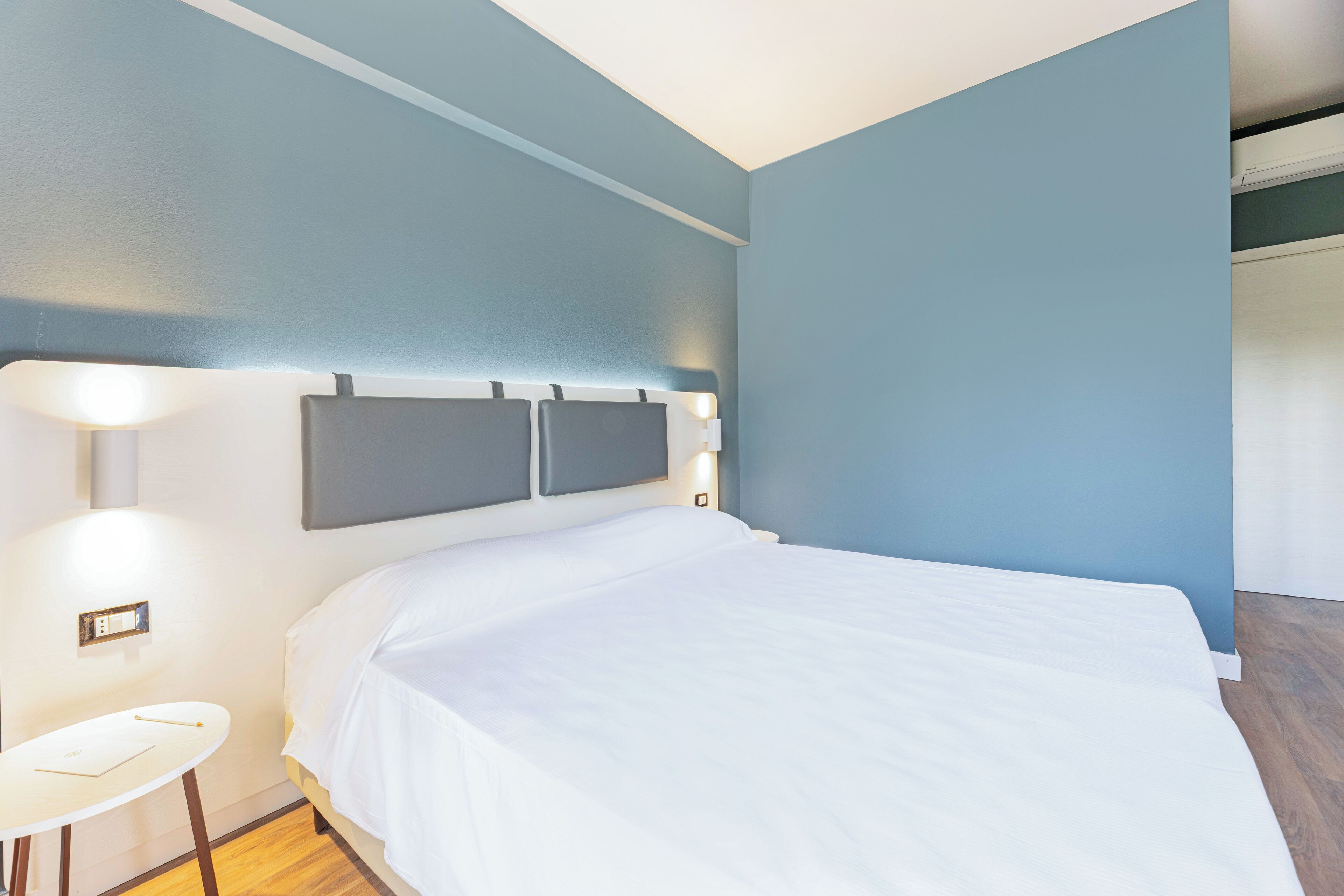 A hotel room with a bed, bedside table, and wall-mounted light fixtures.