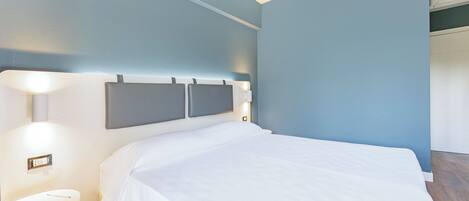 A hotel room with a bed, bedside table, and wall-mounted light fixtures.
