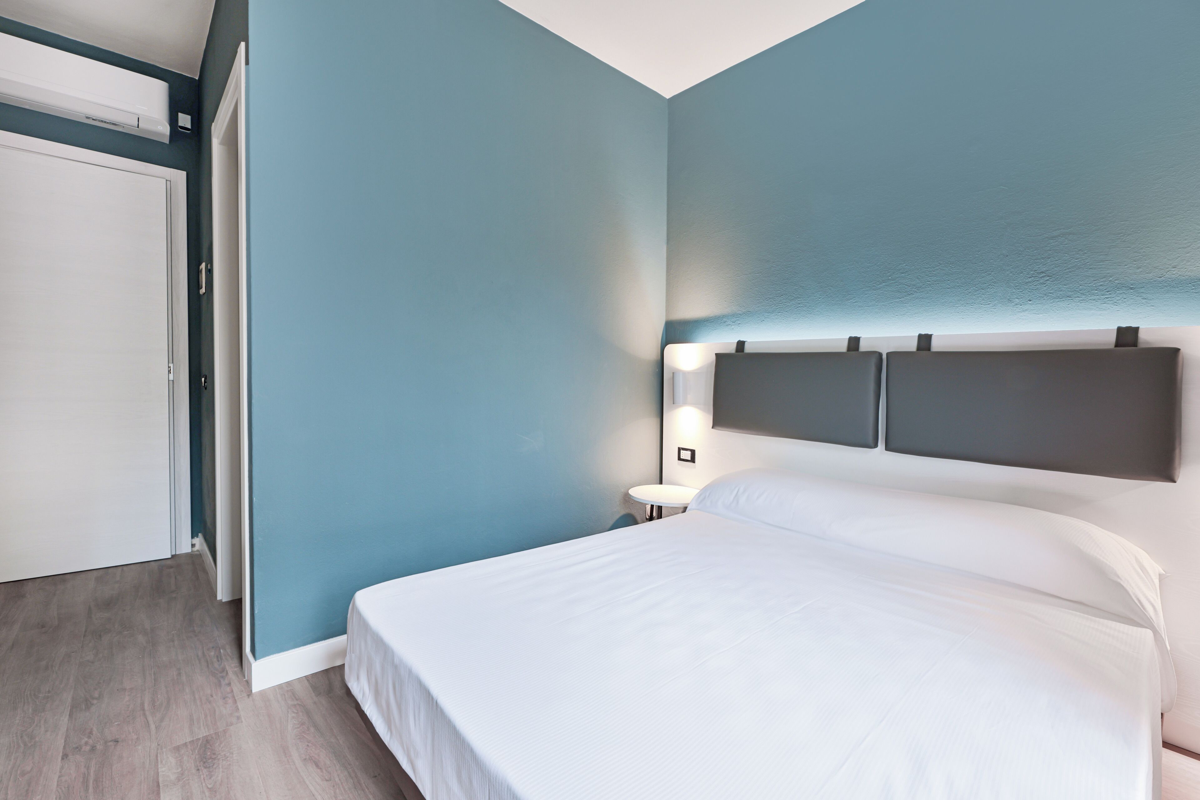 A bedroom with a bed, a nightstand, and a wall-mounted light.