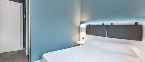 A bedroom with a bed, a nightstand, and a wall-mounted light.