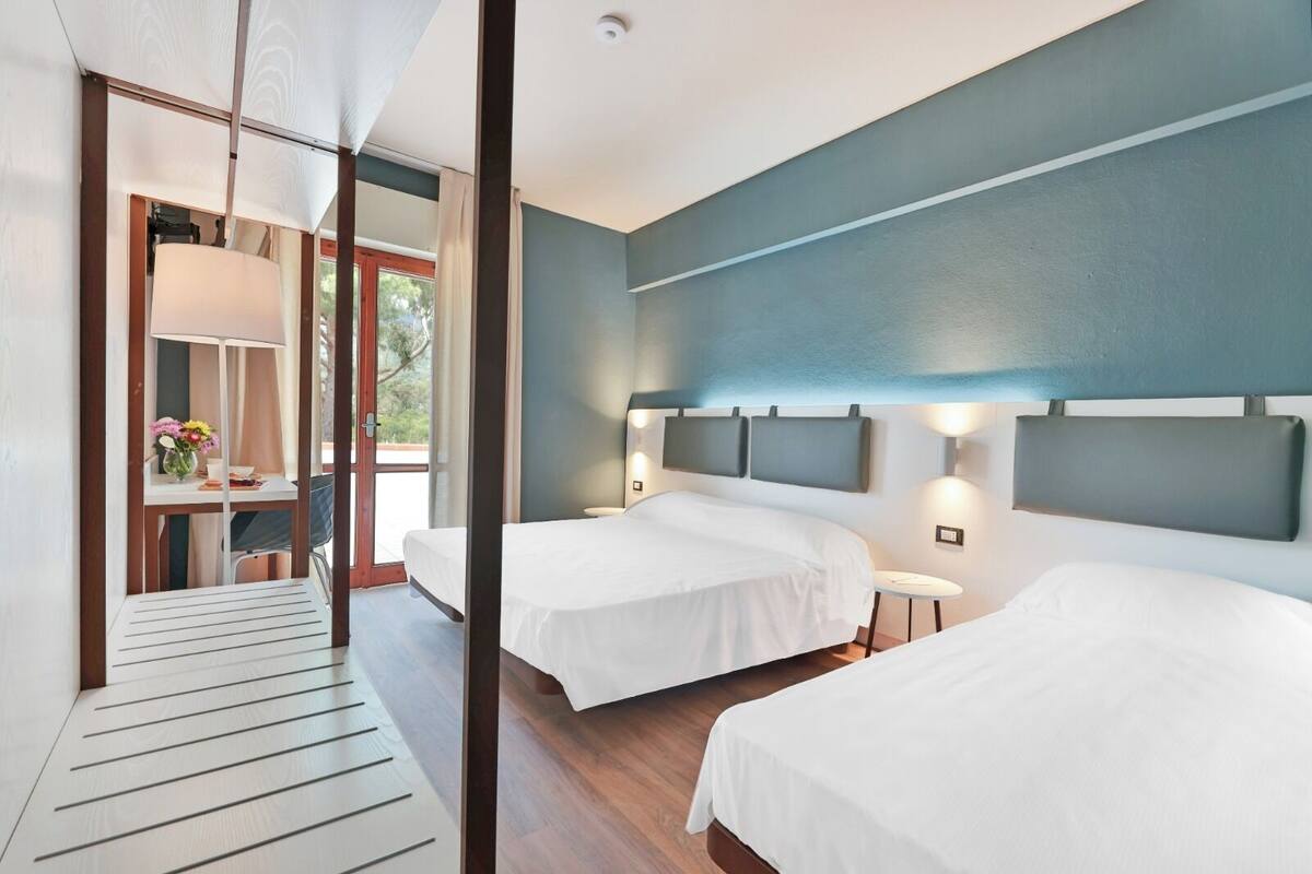 Una habitación de hotel moderna con dos camas, un escritorio con silla y vistas al exterior.