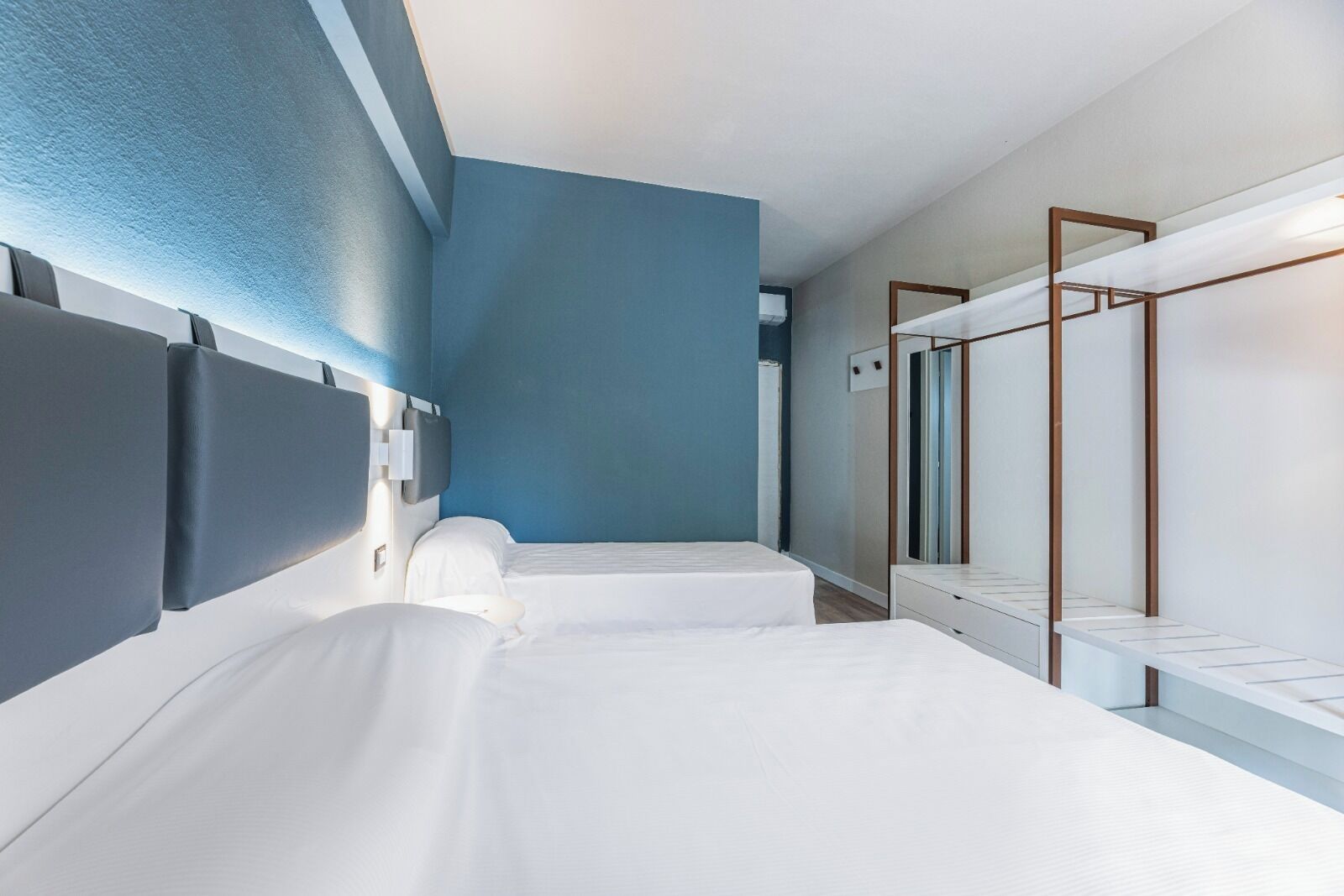 Ein Hotelzimmer mit zwei Betten, einem großen Spiegel und einer blauen Akzentwand.