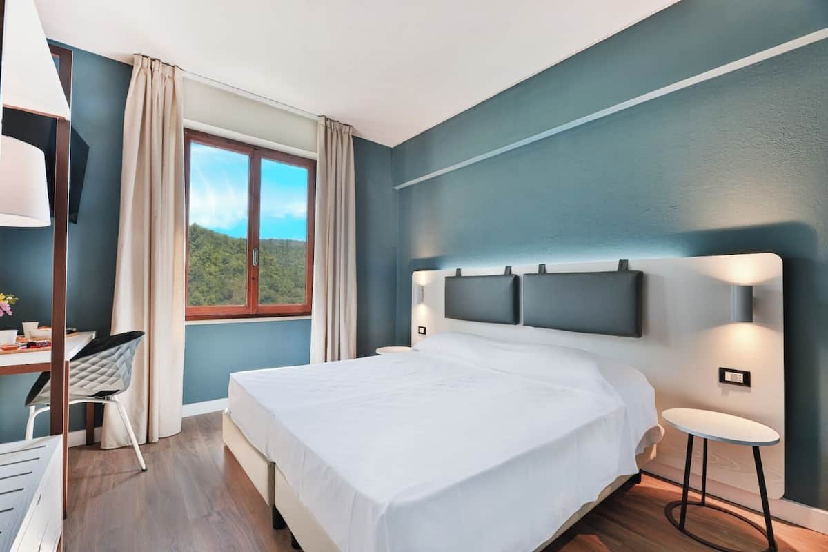Habitación de hotel moderna con una cama grande, un escritorio con silla y vistas al exterior a través de una ventana.