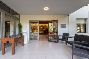 A room with a foosball table, a sofa, and a chair. There is a door leading to another room with a Christmas tree and a sign that says "The Lounge". - Elba Vibe Smart Hotel (Campo nell'Elba)