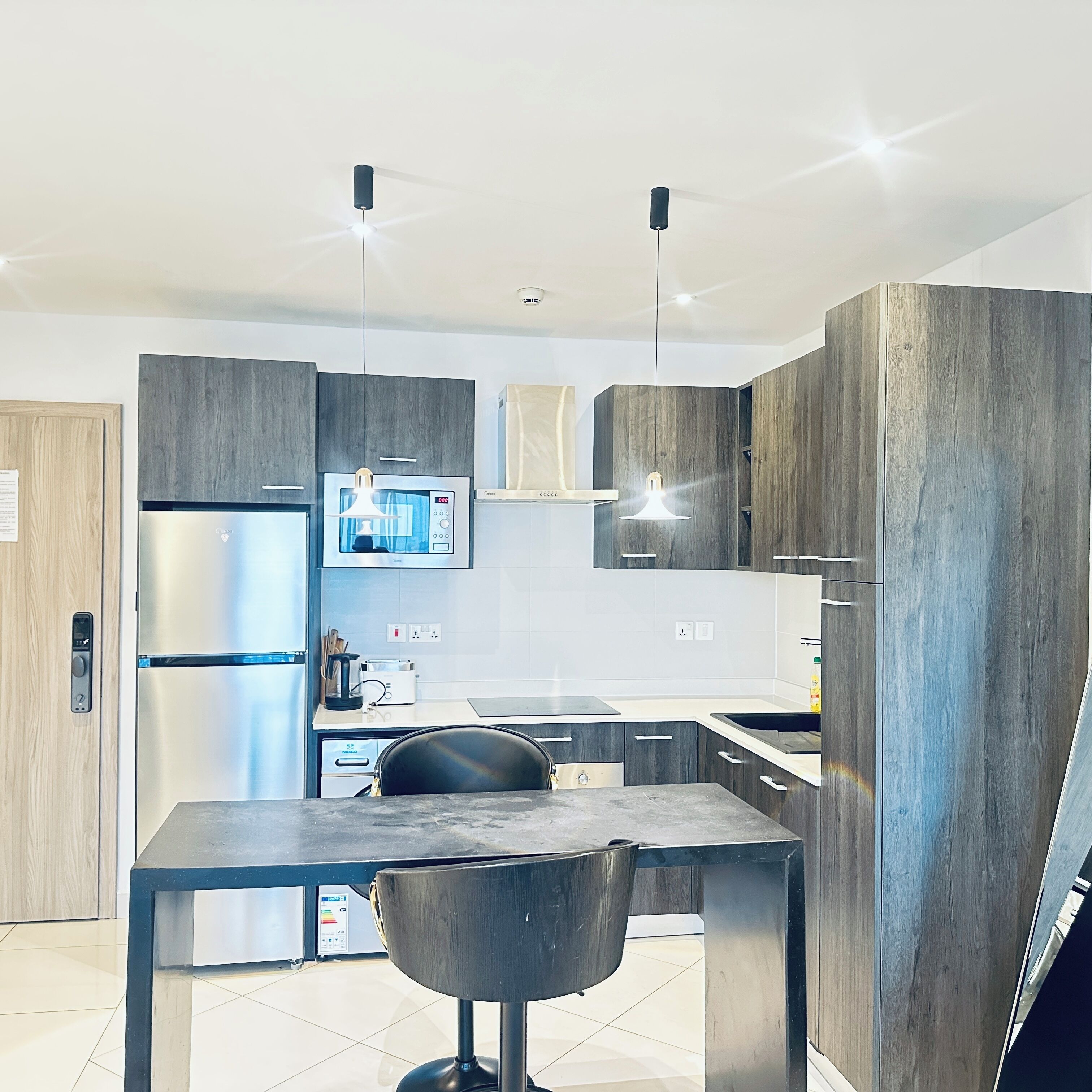 Una cocina moderna con refrigerador integrado, cafetera y comedor con mesa y silla.