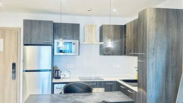 Una cocina moderna con refrigerador integrado, cafetera y comedor con mesa y silla.