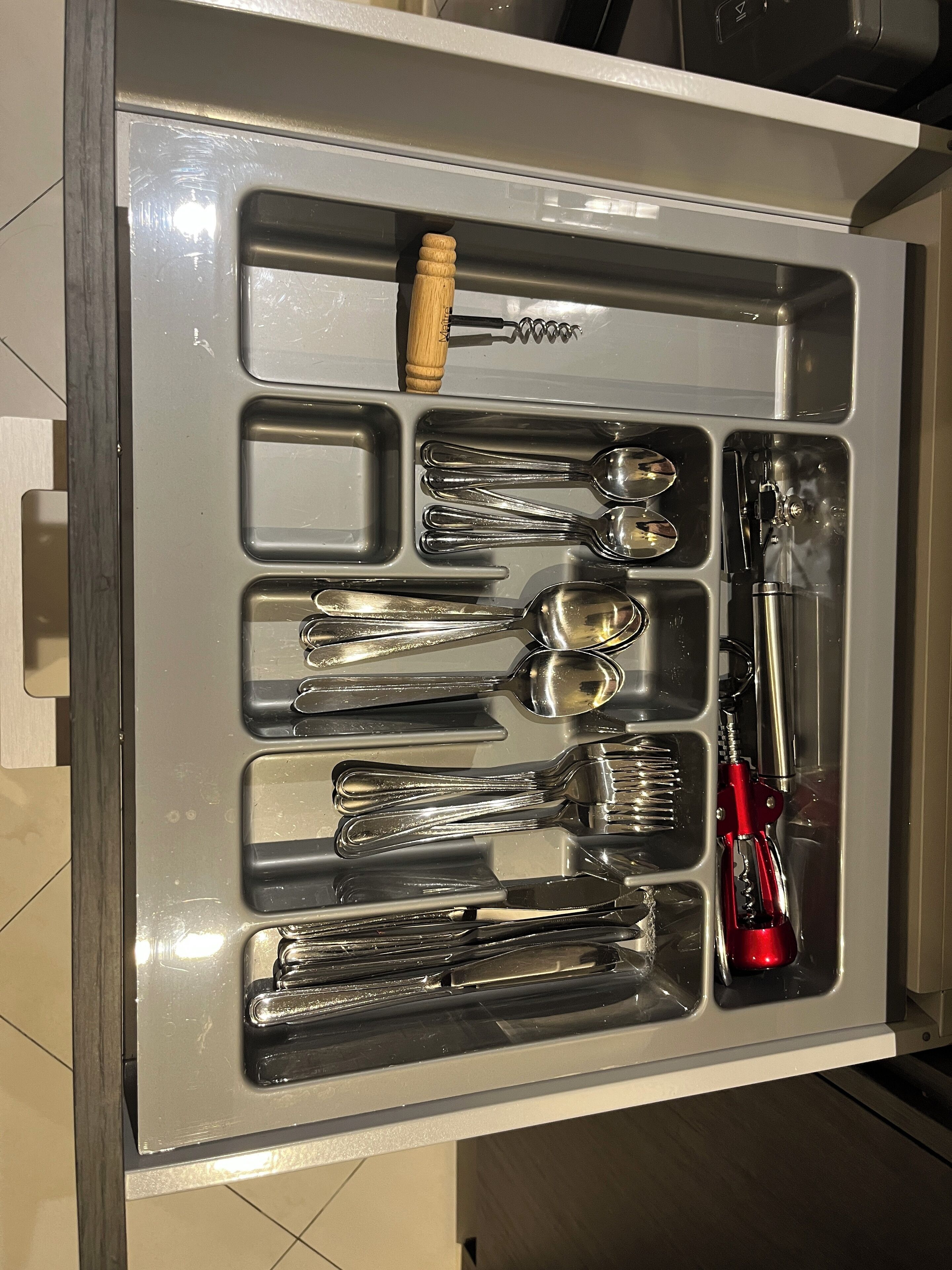 A drawer with compartments containing various kitchen utensils including spoons, forks, and a red-handled tool.