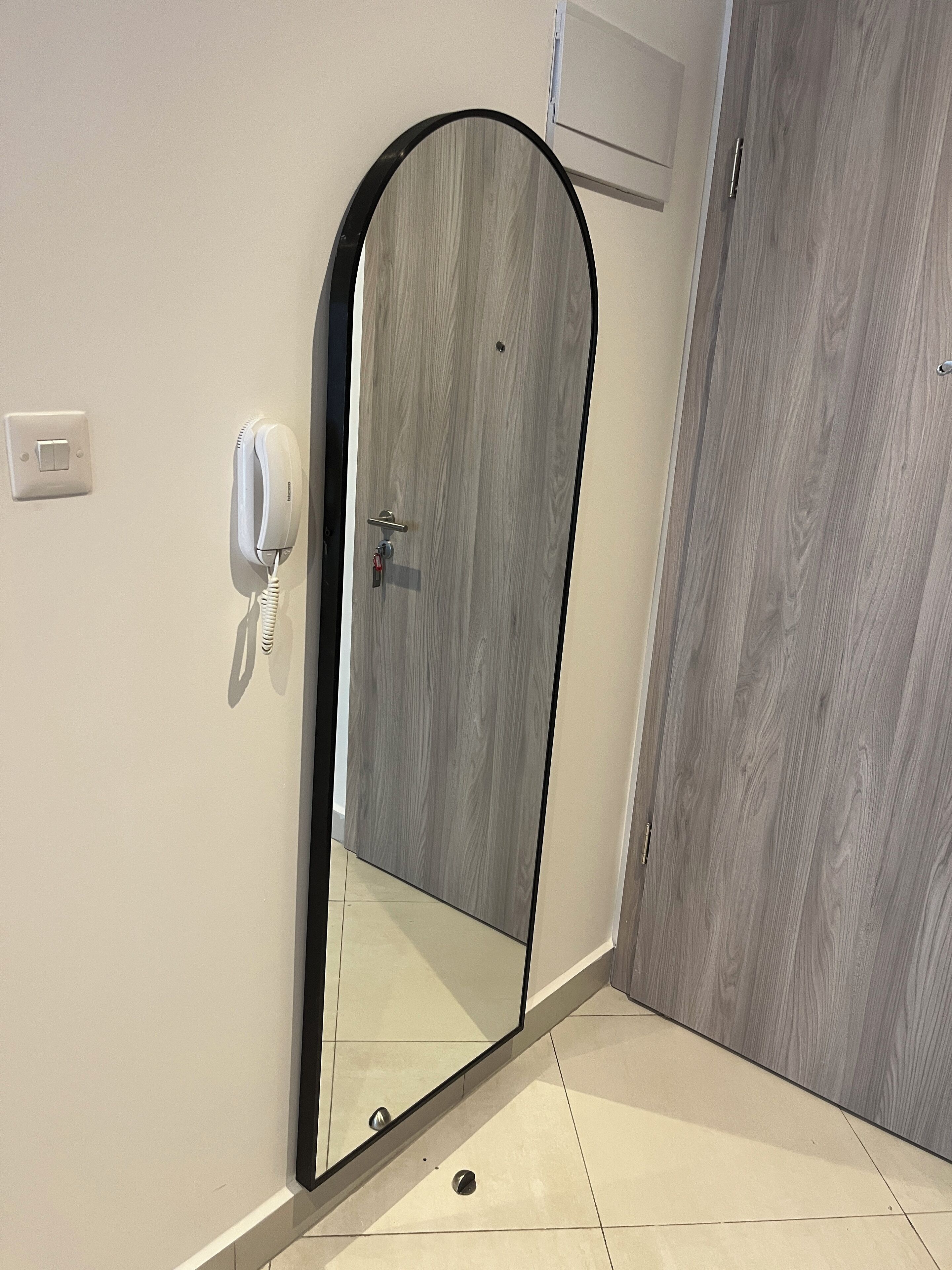 A modern bathroom with a large mirror, a white wall-mounted phone, and a wooden door.