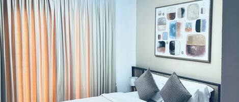 A modern hotel room with a neatly made bed, a wall-mounted abstract art piece, and a ceiling light fixture.