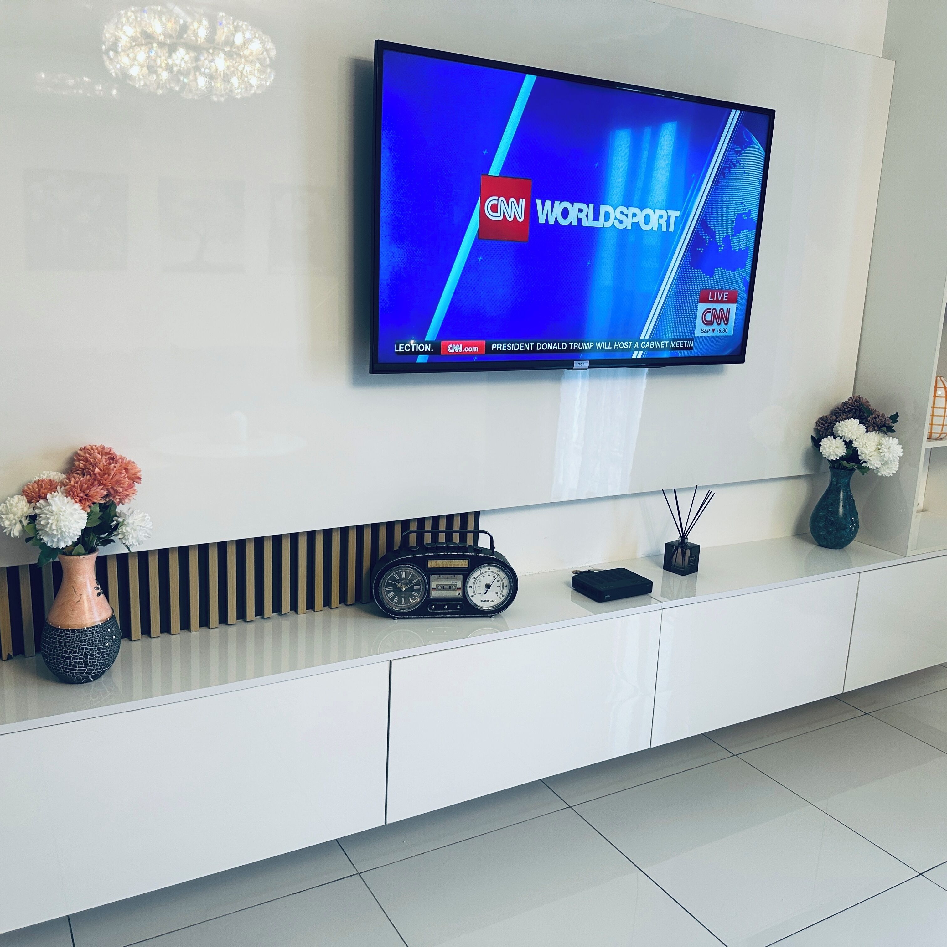 A modern living room with a flat-screen TV mounted on the wall displaying CNN World Sport.