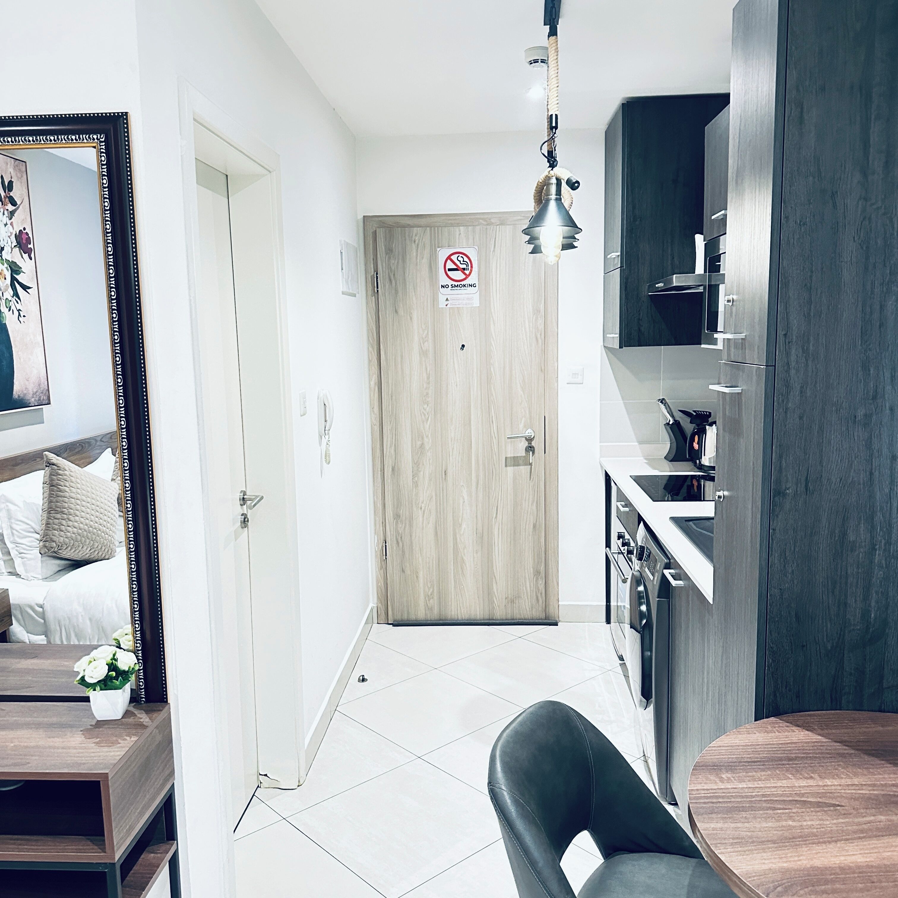 Ett modernt kök med en inbyggd ugn, en matplats med bord och stolar samt en hall som leder till en dörr med en skylt som säger ”Rökning förbjuden”.