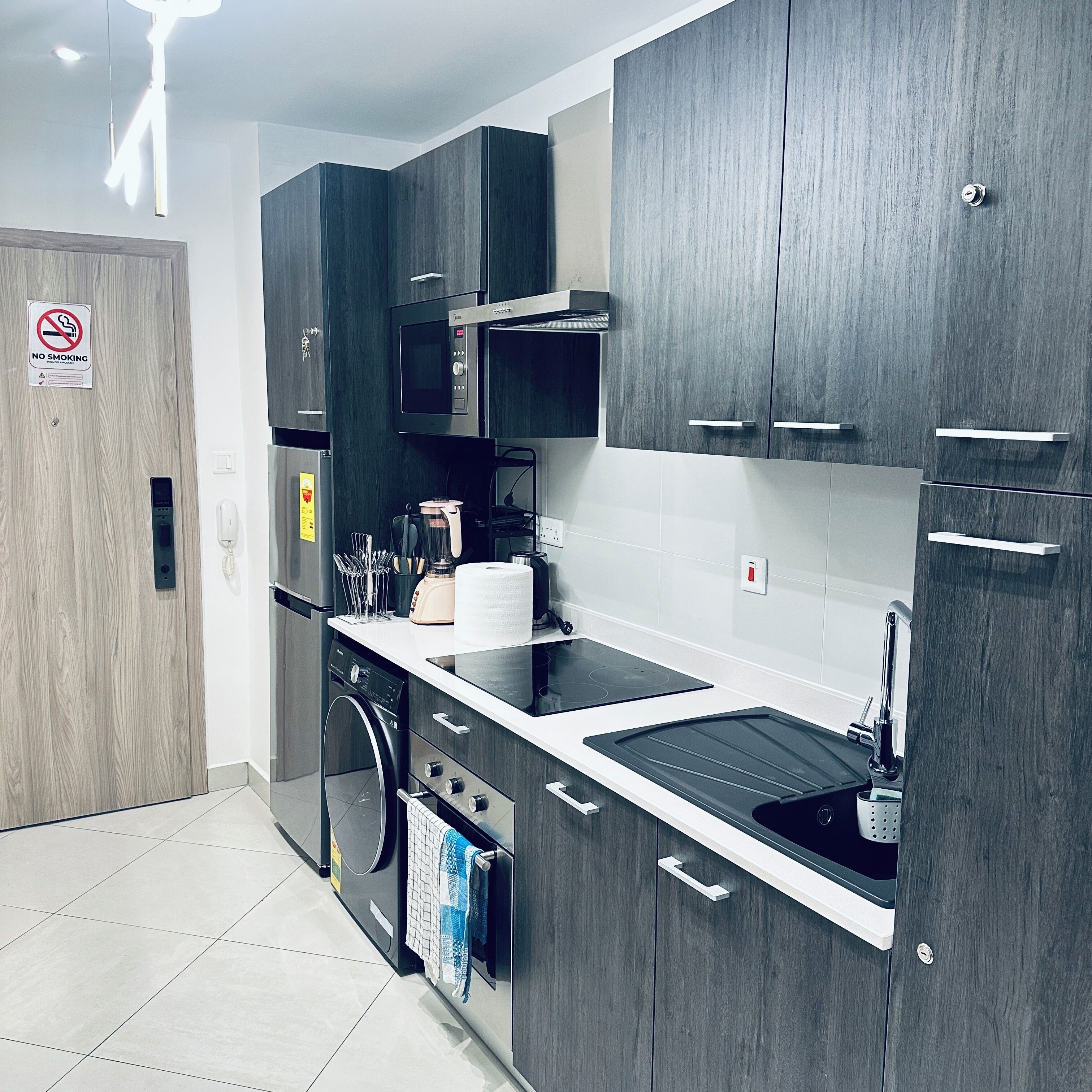 A modern kitchen with dark wood cabinets, a stainless steel refrigerator, a microwave, and a built-in oven.