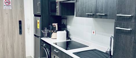 A modern kitchen with dark wood cabinets, a stainless steel refrigerator, a microwave, and a built-in oven.