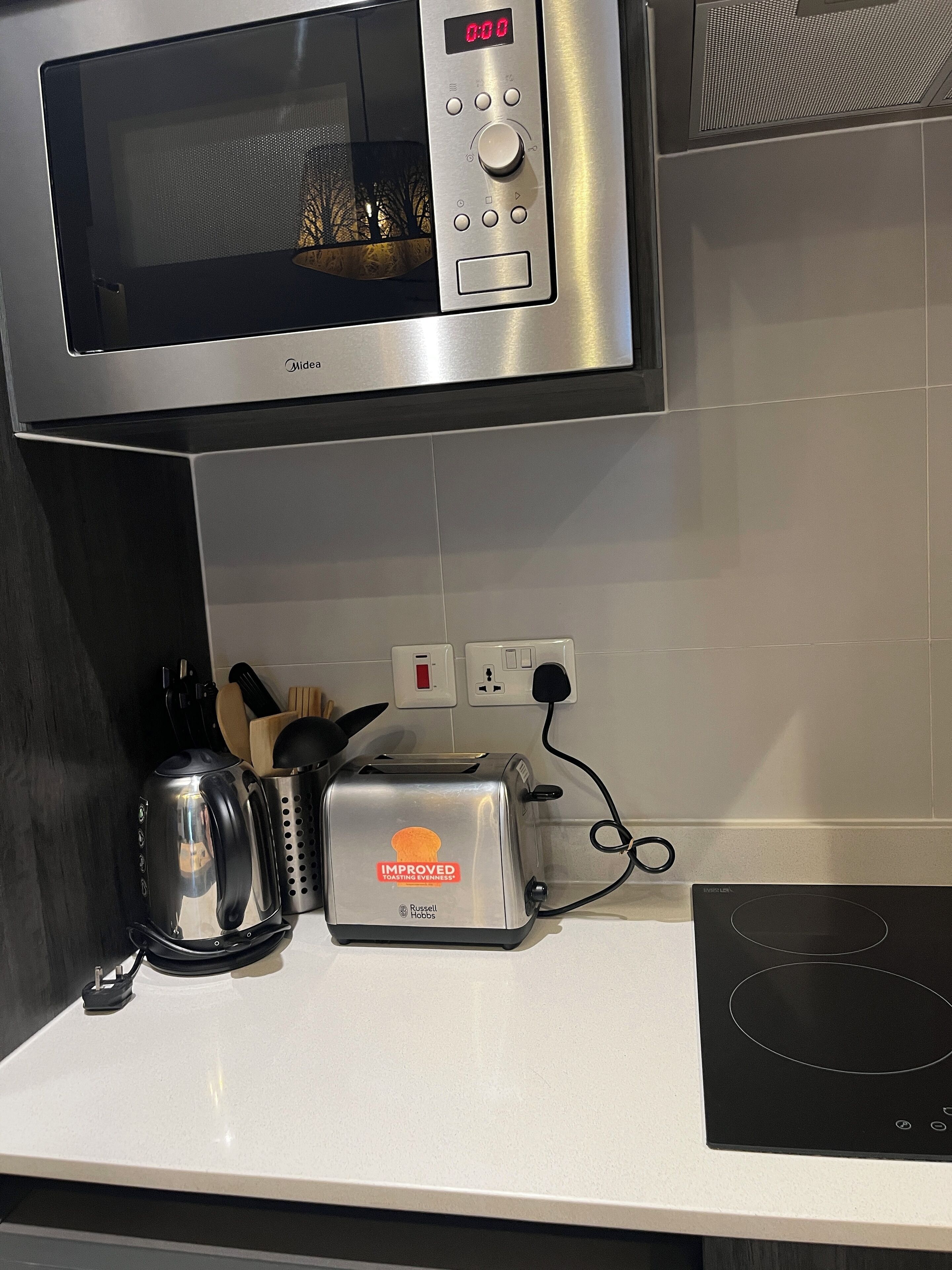 Una cocina con microondas, tostadora, hervidor y una placa de inducción negra.