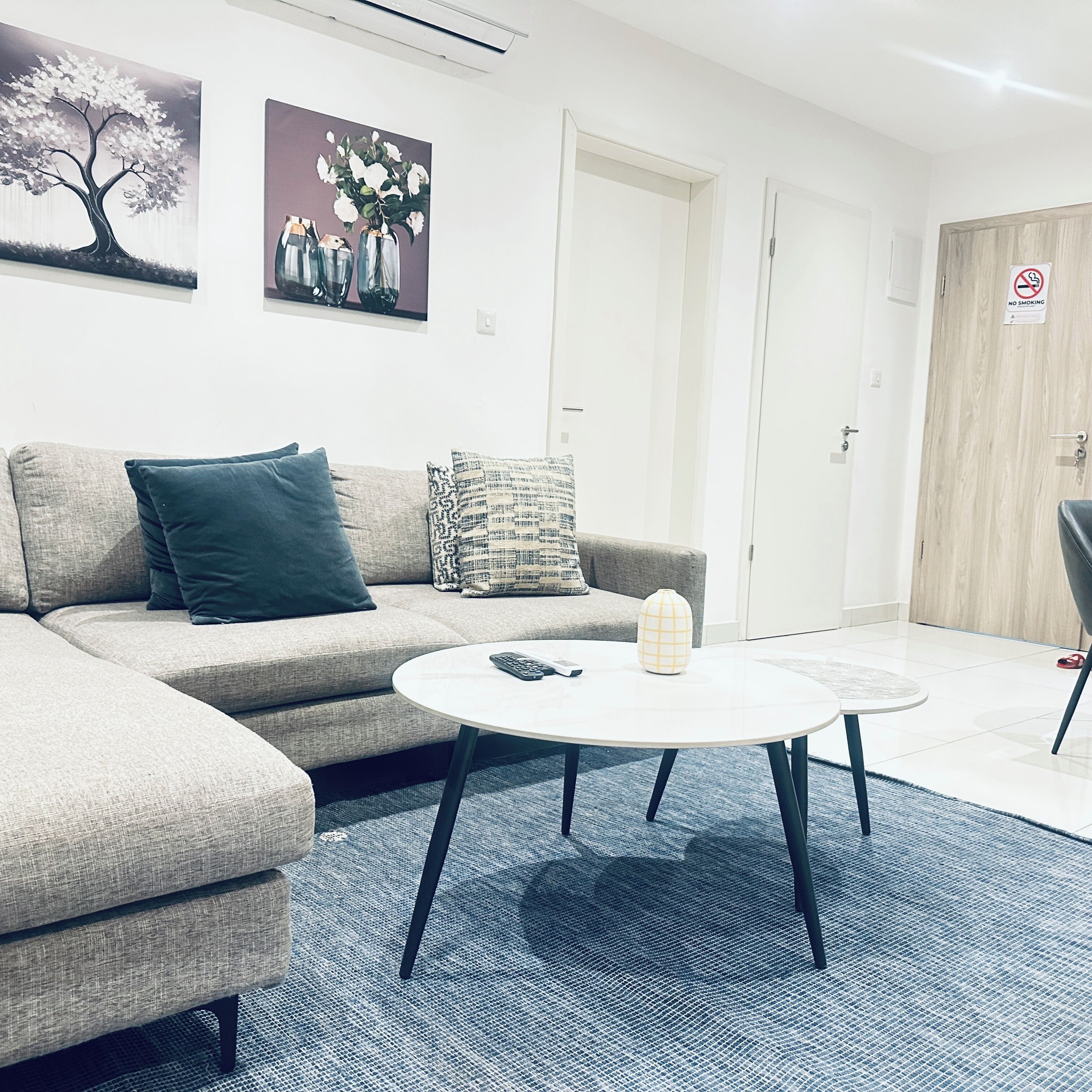 Un salón moderno con un sofá gris, una mesa de centro redonda y un cuadro de flores en la pared.