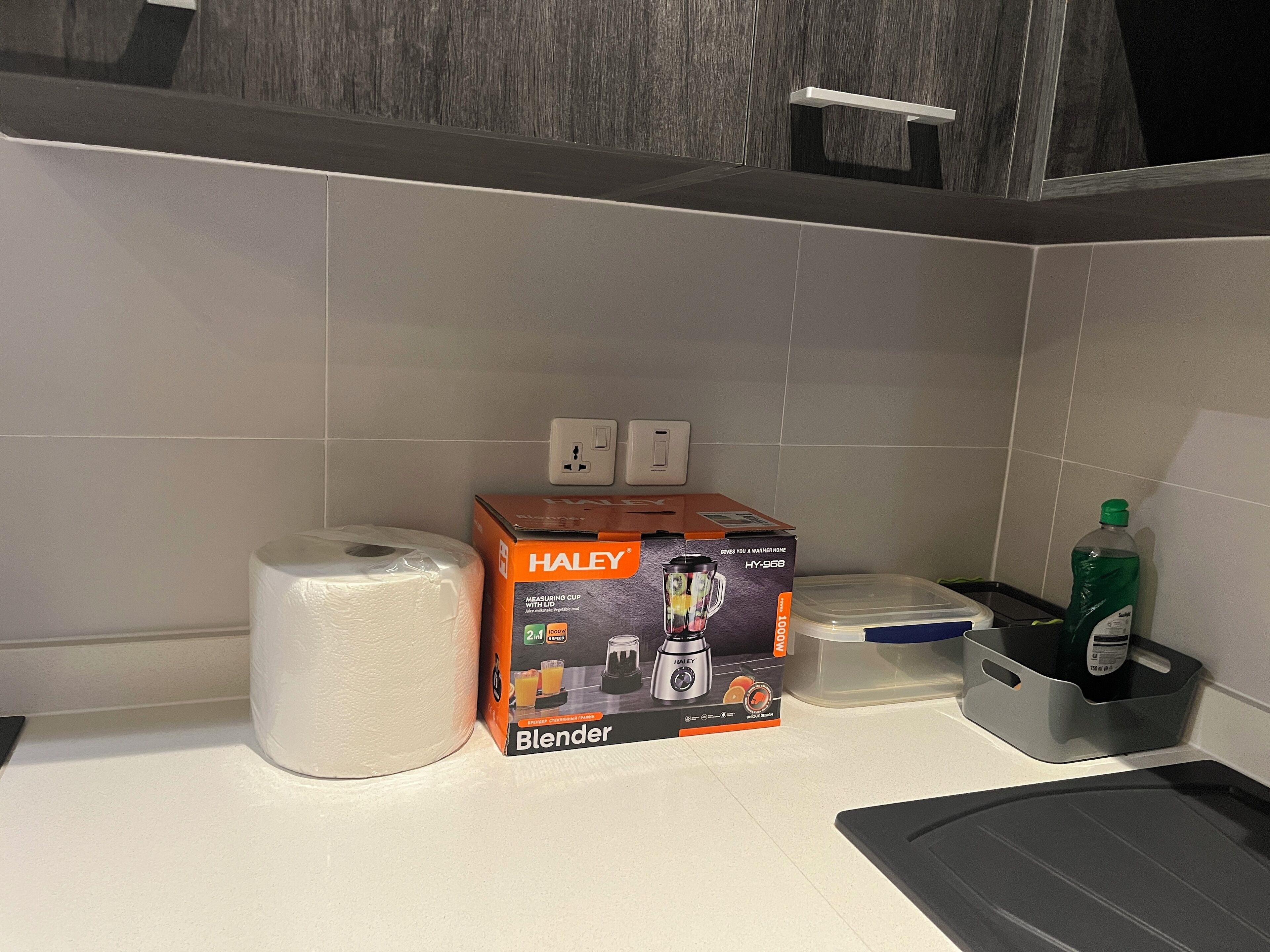 Una cocina con una caja de licuadora, un rollo de toallas de papel y un recipiente de plástico.
