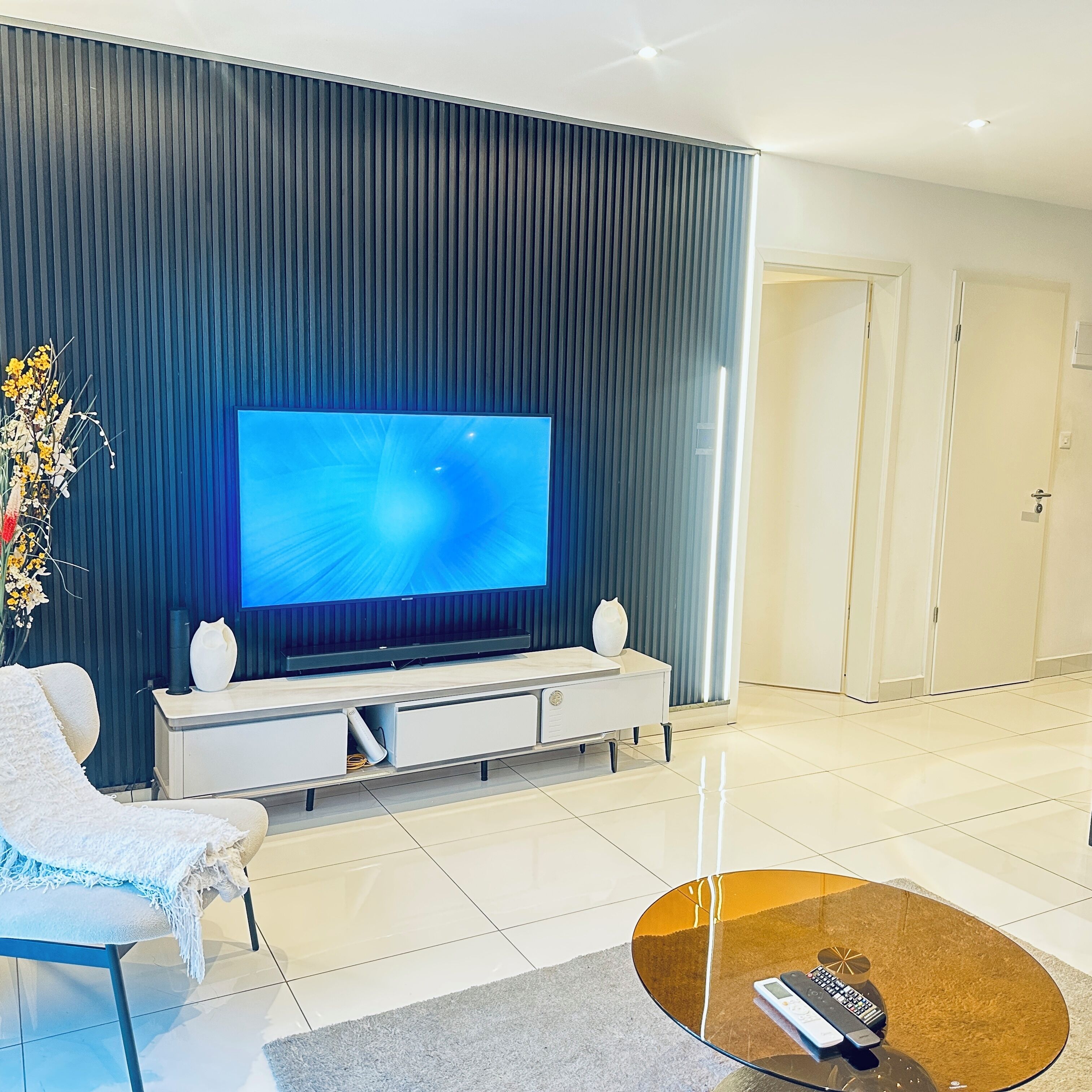 Uma sala de estar moderna com uma televisão de tela plana, um sofá branco, uma mesa de centro e um vaso decorativo.