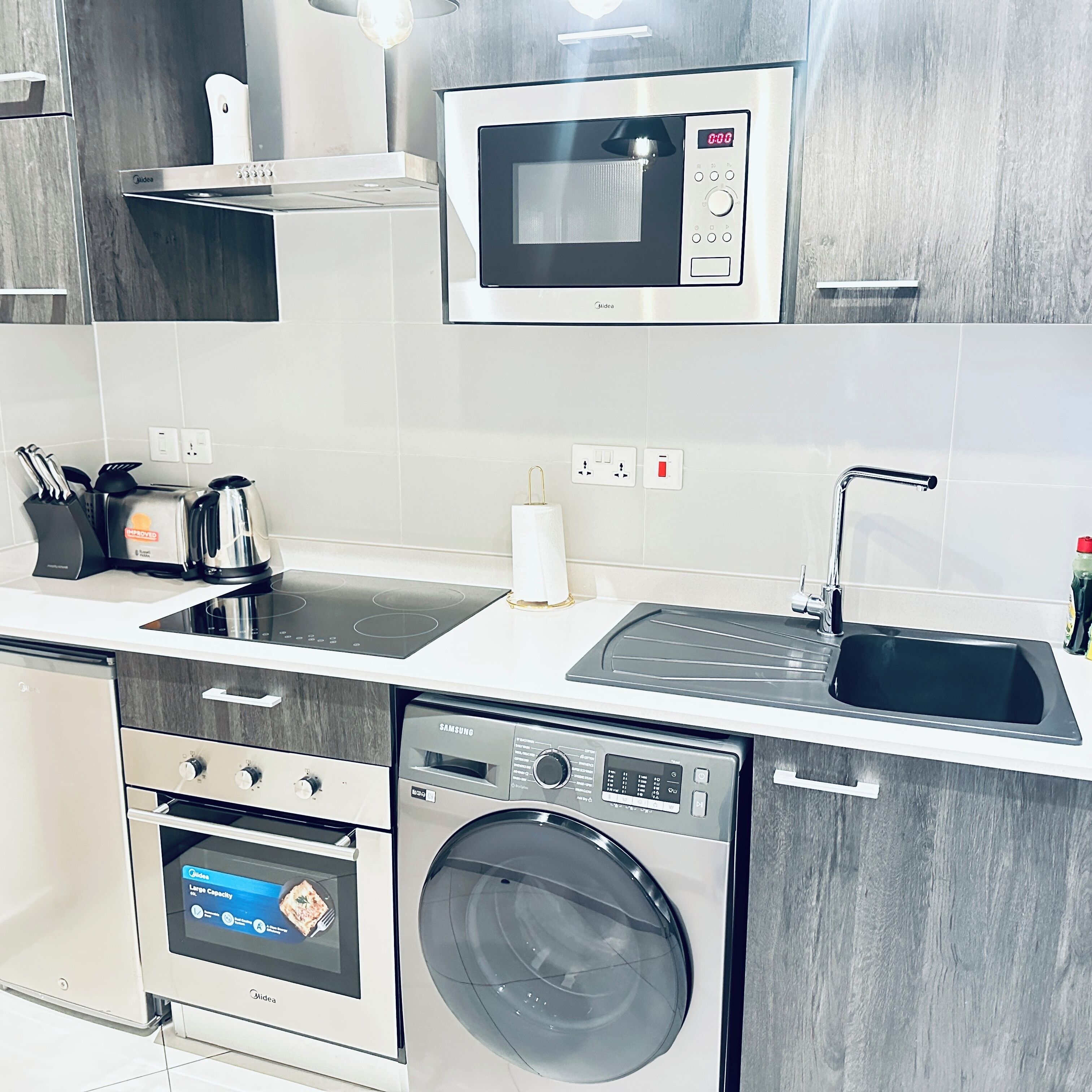 A modern kitchen with a built-in microwave, toaster, sink, and washing machine.