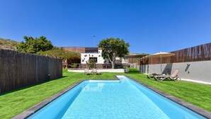 A rectangular swimming pool with a clear blue water surface, surrounded by a wooden fence and a grassy lawn.