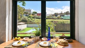 A dining table with plates, cutlery, and glasses, set against a window overlooking a backyard with a pool and greenery.